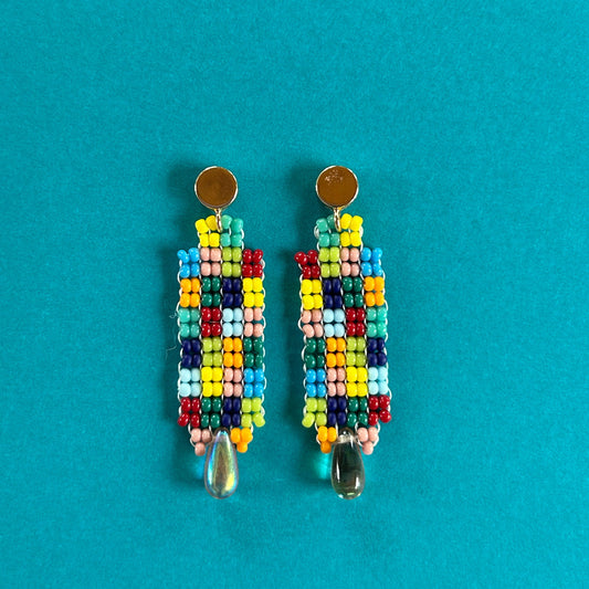 A pair of handmade beaded dangle earrings with gold-tone studs and clear teardrop charms, displayed on a solid teal background.