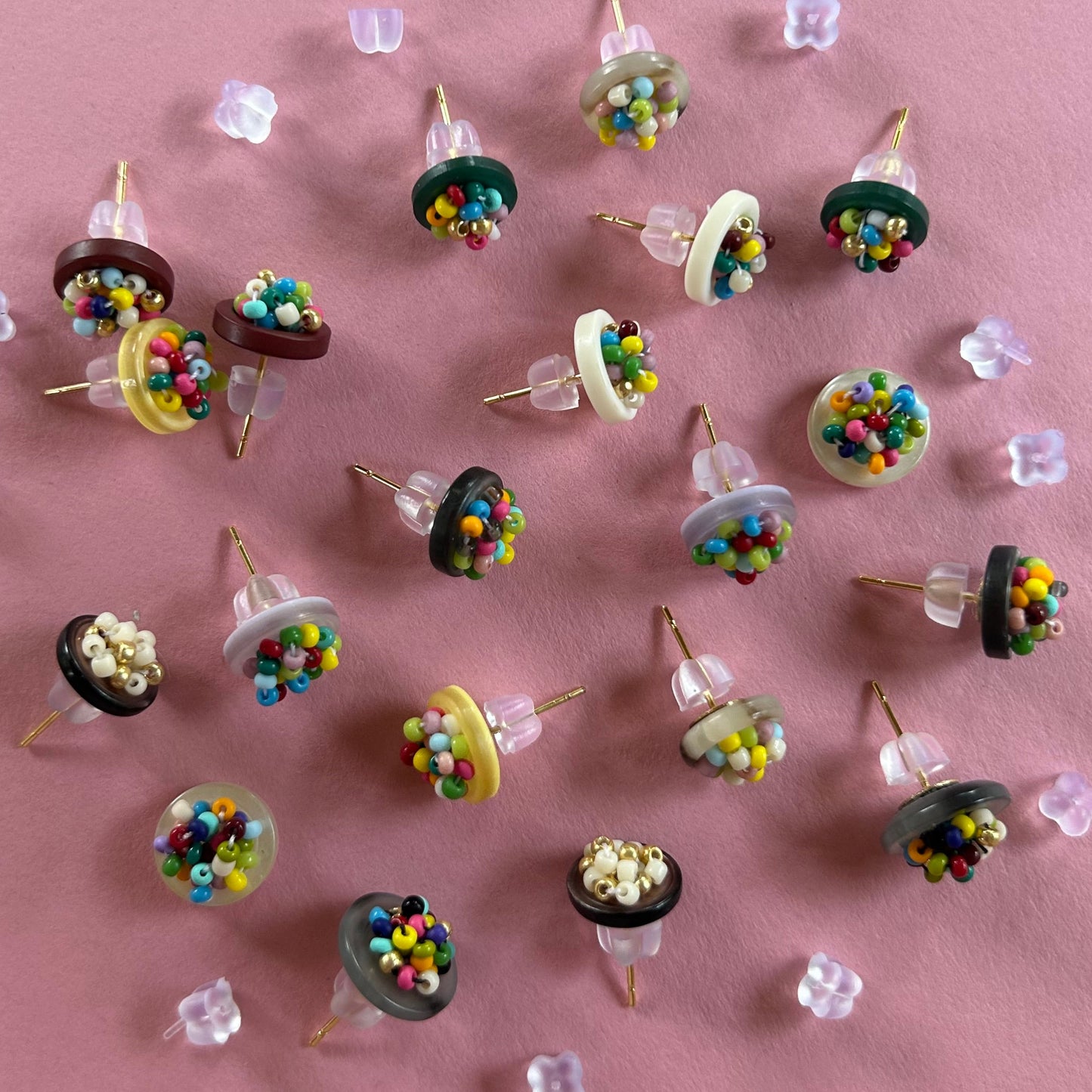 A collection of miniature novelty earrings shaped like miniature cupcakes, arranged on a solid pink background.