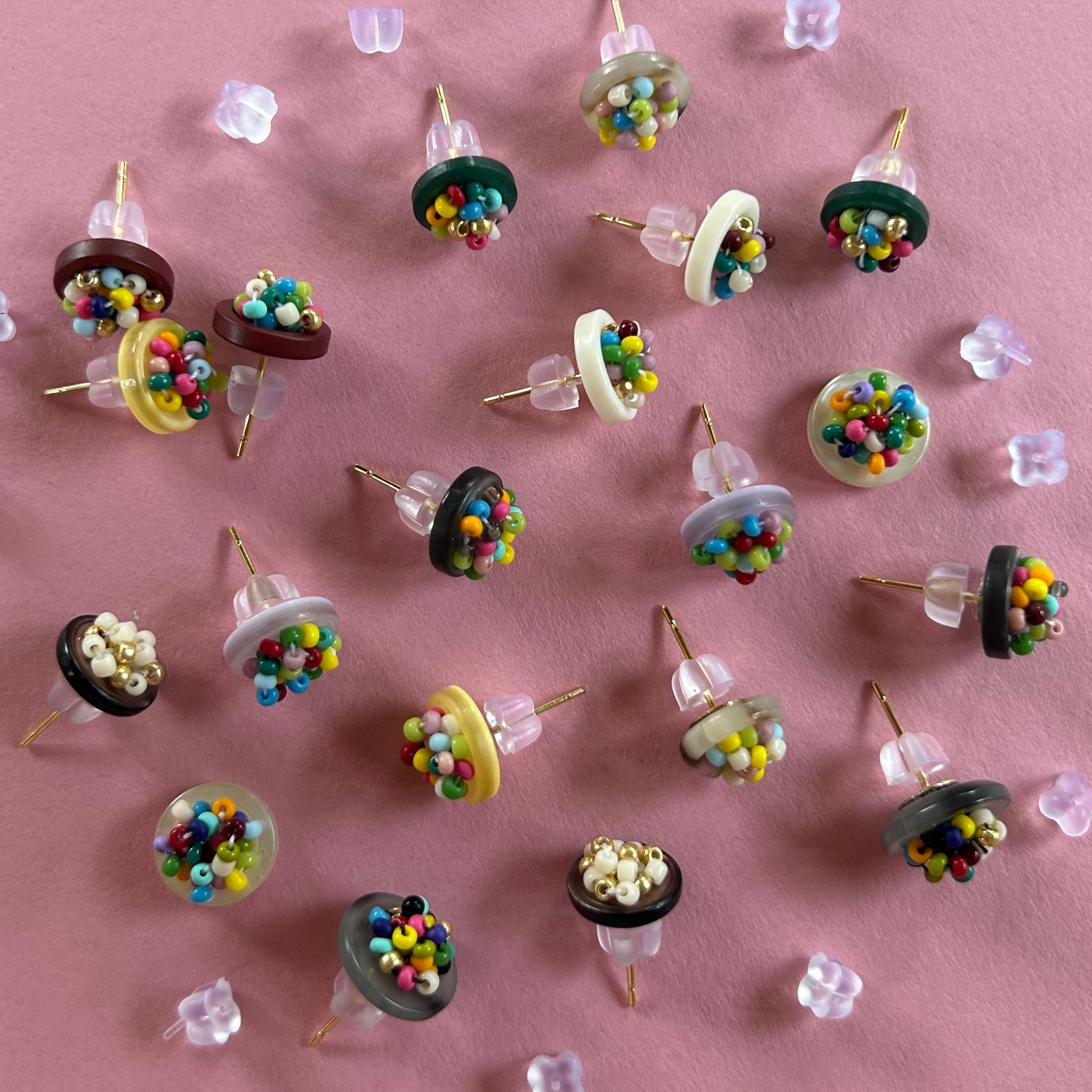 A collection of miniature novelty earrings shaped like miniature cupcakes, arranged on a solid pink background.